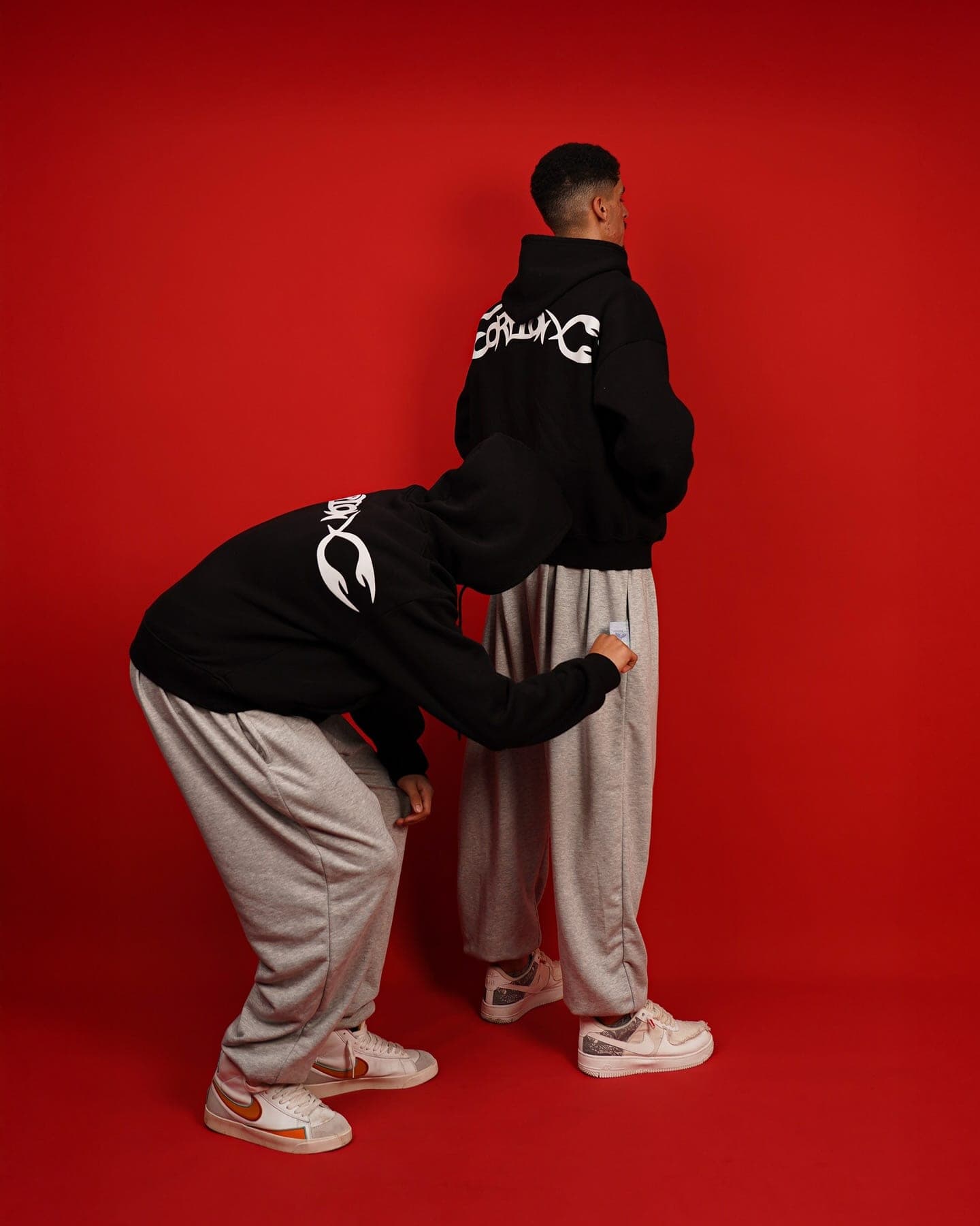 Two crew members on a red backdrop, ScorpionX back prints and grey Toji Sweatpants