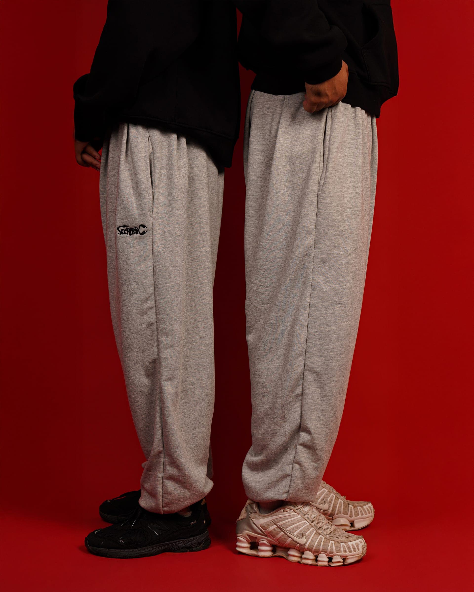 Two pairs of grey Toji Sweatpants against a red backdrop