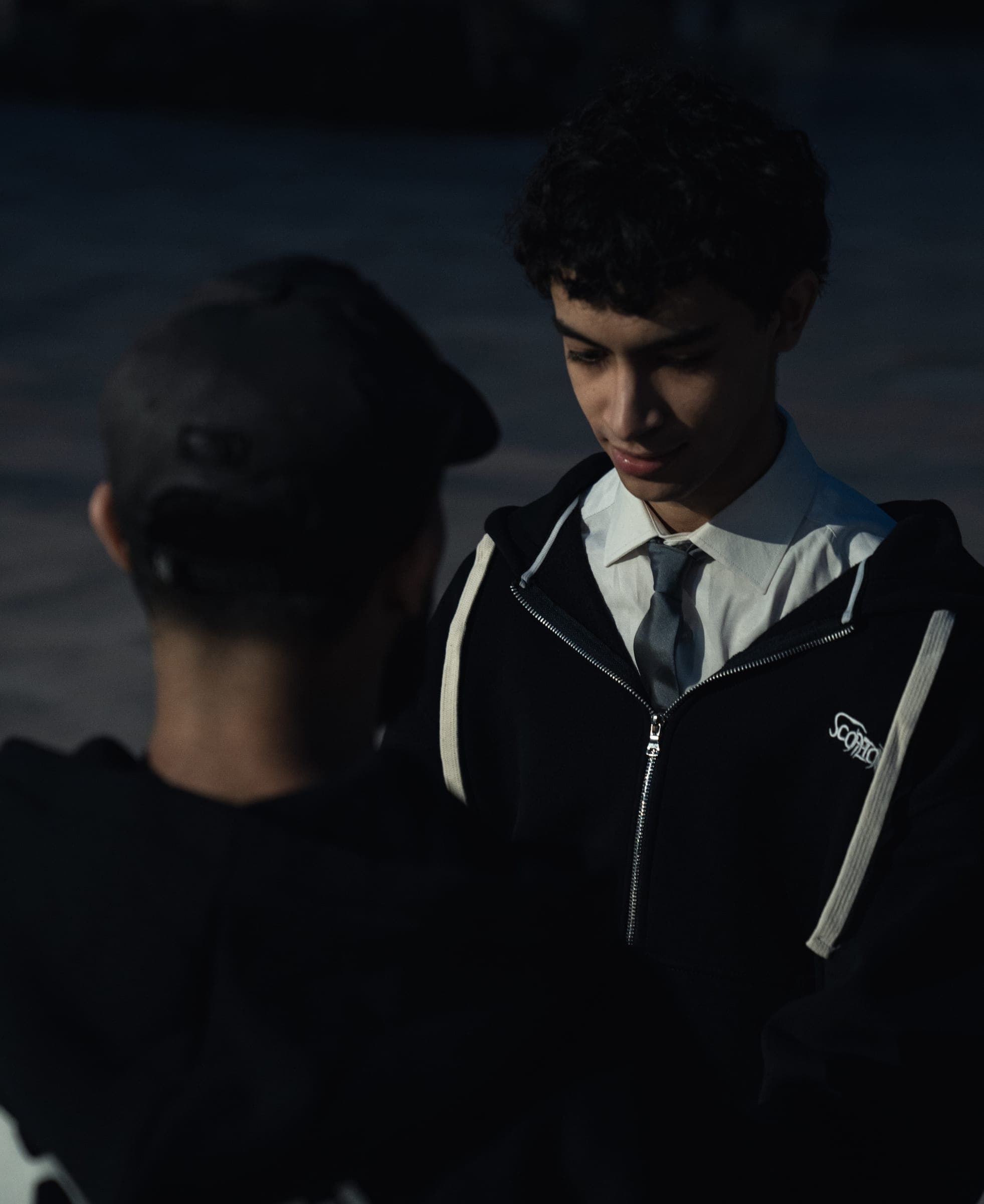 Close-up at night: the zip-up hoodie worn over a white shirt and tie