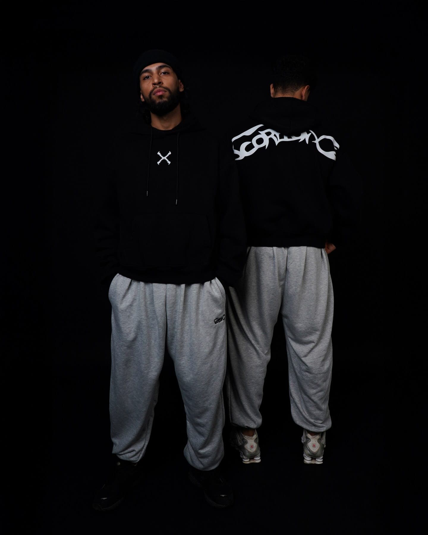 Two crew members on black, one with the X on the chest, one showing the back print, both in grey Toji Sweatpants